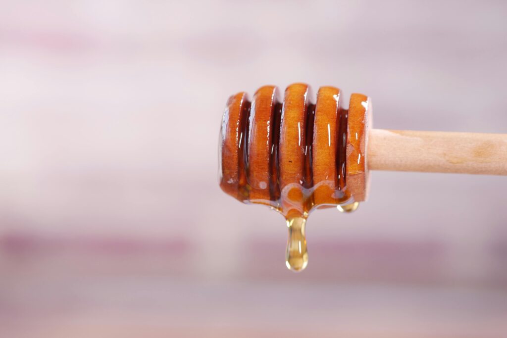 Close-up of honey dripping from a wooden dipper, capturing the sweet, sticky texture.