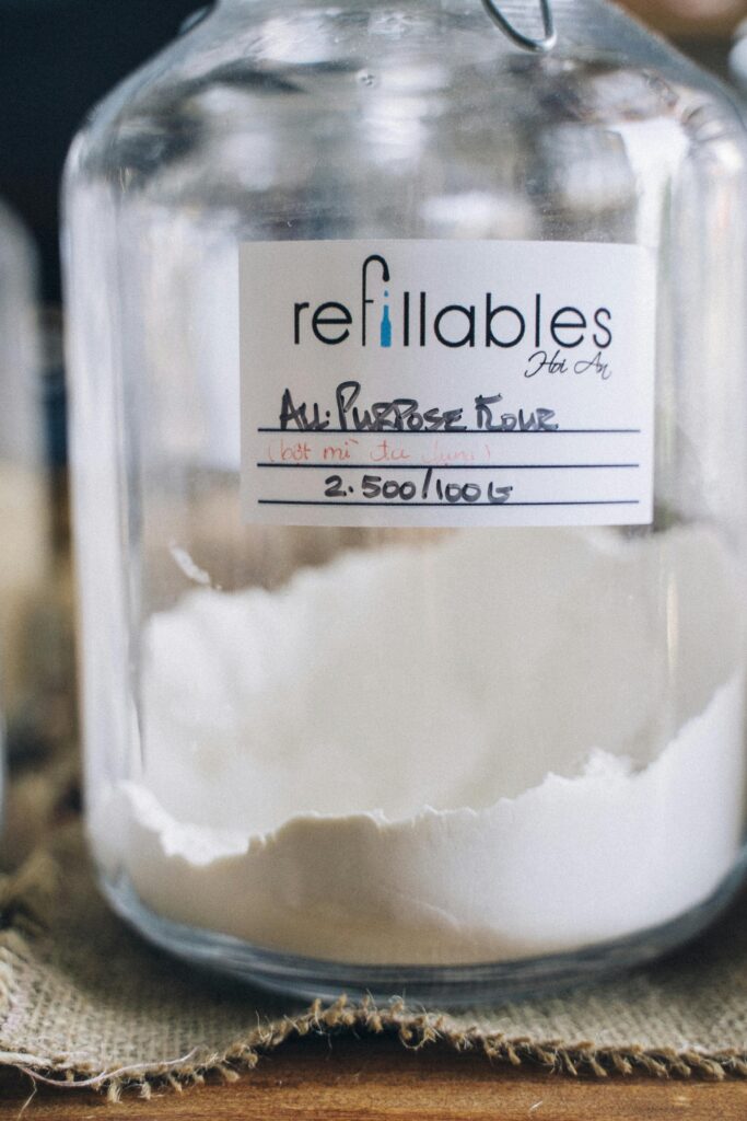 Clear glass jar with all-purpose flour displaying eco-friendly refill label.